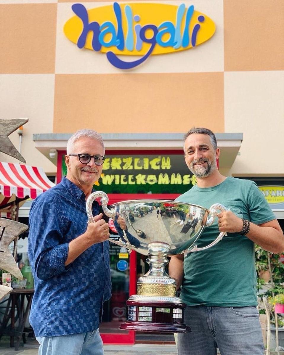 Zwei Männer mit einem großen Pokal unter dem Halligalli-Schriftzug — Beitrag von @kipagmbh2022