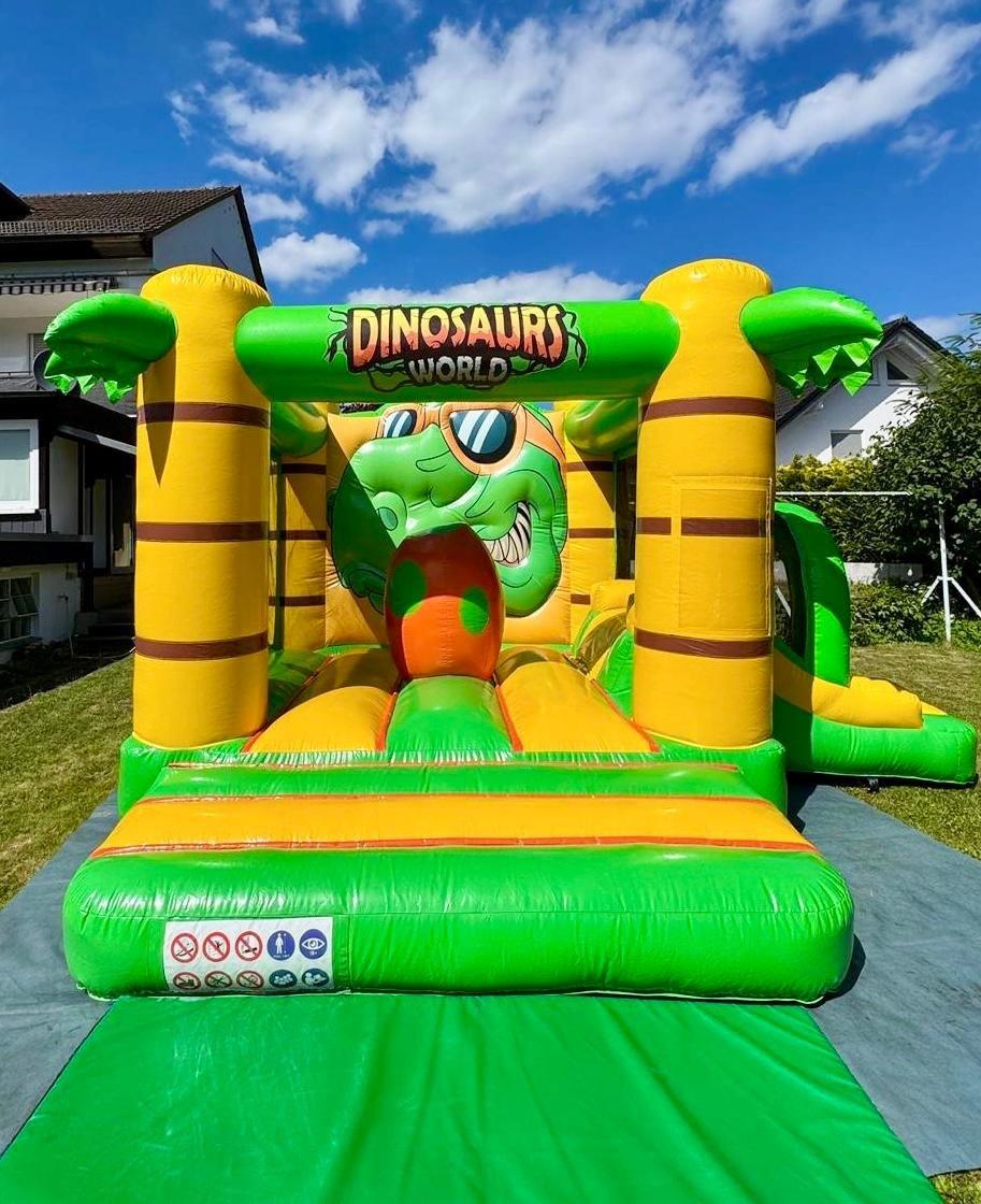 Große Hüpfburg im Dinosaurier-Design auf einer Wiese
